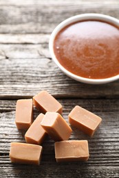 Yummy candies and caramel sauce in bowl on wooden table, closeup