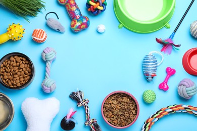 Different pet toys and feeding bowls on light blue background, flat lay. Space for text