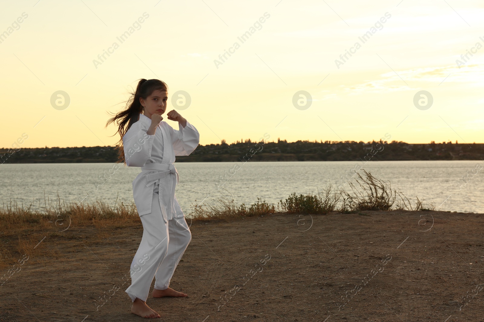 Photo of Cute little girl in kimono practicing karate near river at sunset