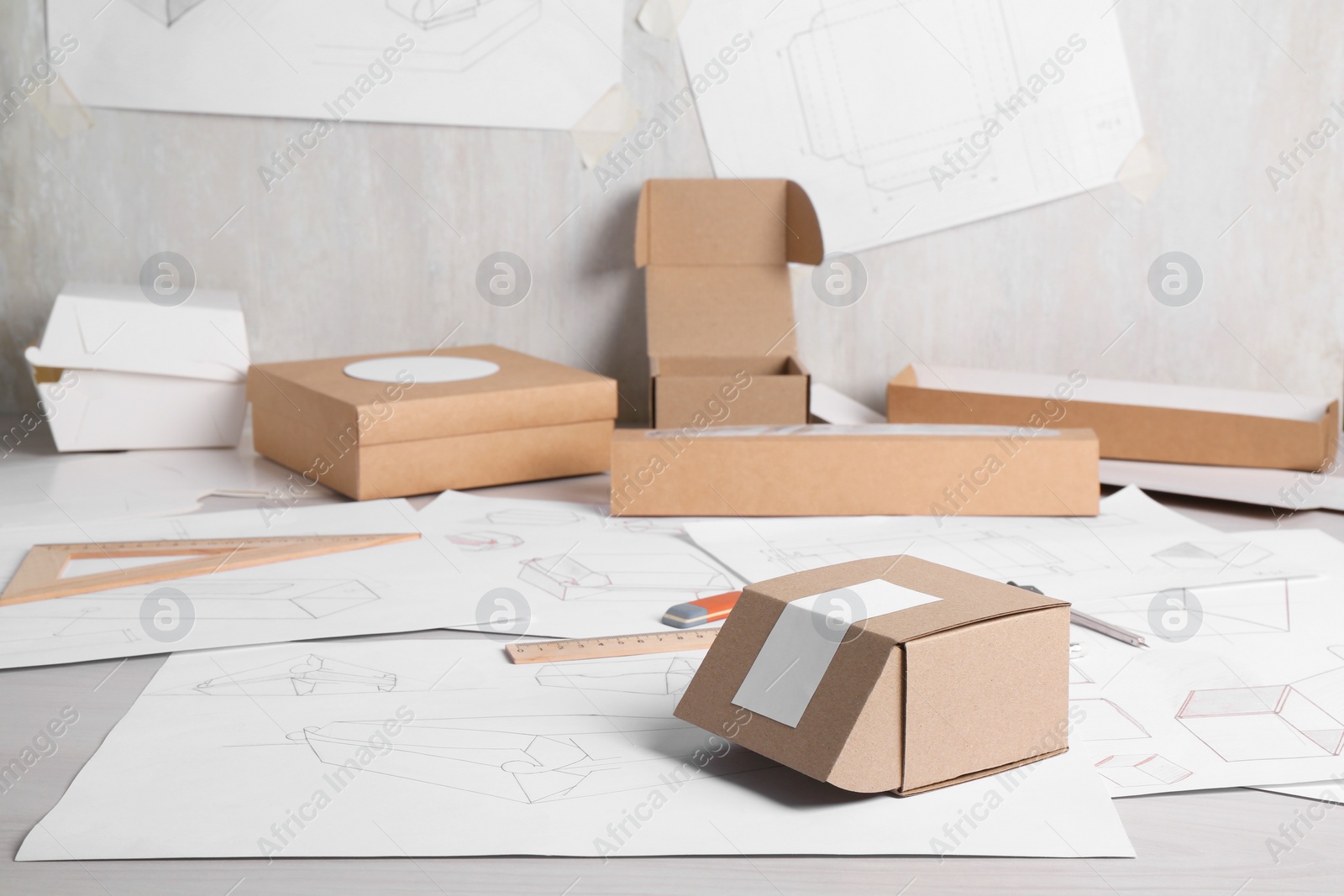 Photo of Creating packaging design. Drawings, boxes and stationery on light wooden table, closeup