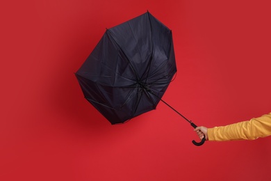 Man holding umbrella caught in gust of wind on red background, closeup