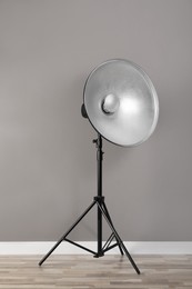 Photo of Professional beauty dish reflector on tripod near grey wall in room. Photography equipment
