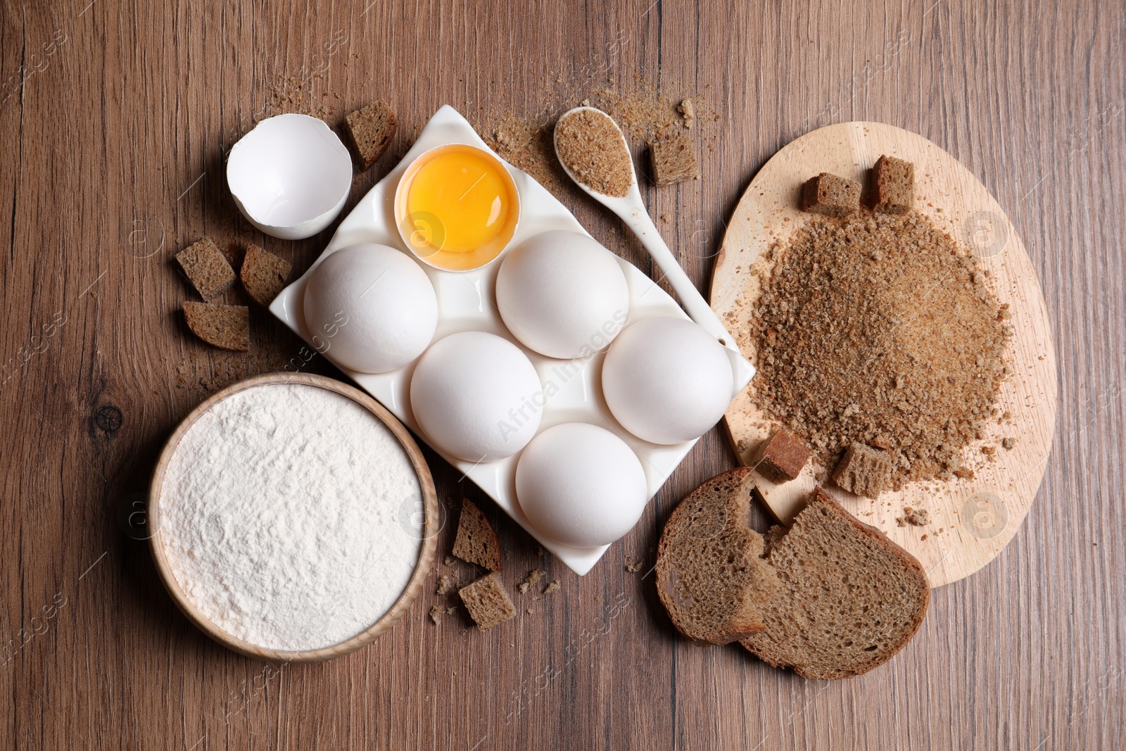 Photo of Fresh breadcrumbs, flour and eggs on wooden table, flat lay