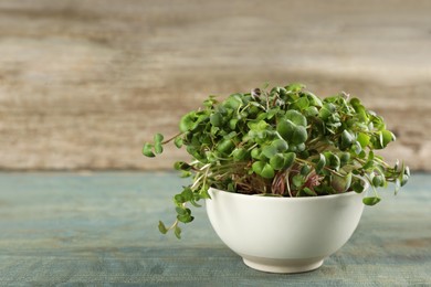 Photo of Fresh radish microgreens in bowl on light blue wooden table, space for text