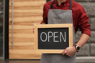 Young male business owner holding OPEN sign near his cafe, closeup