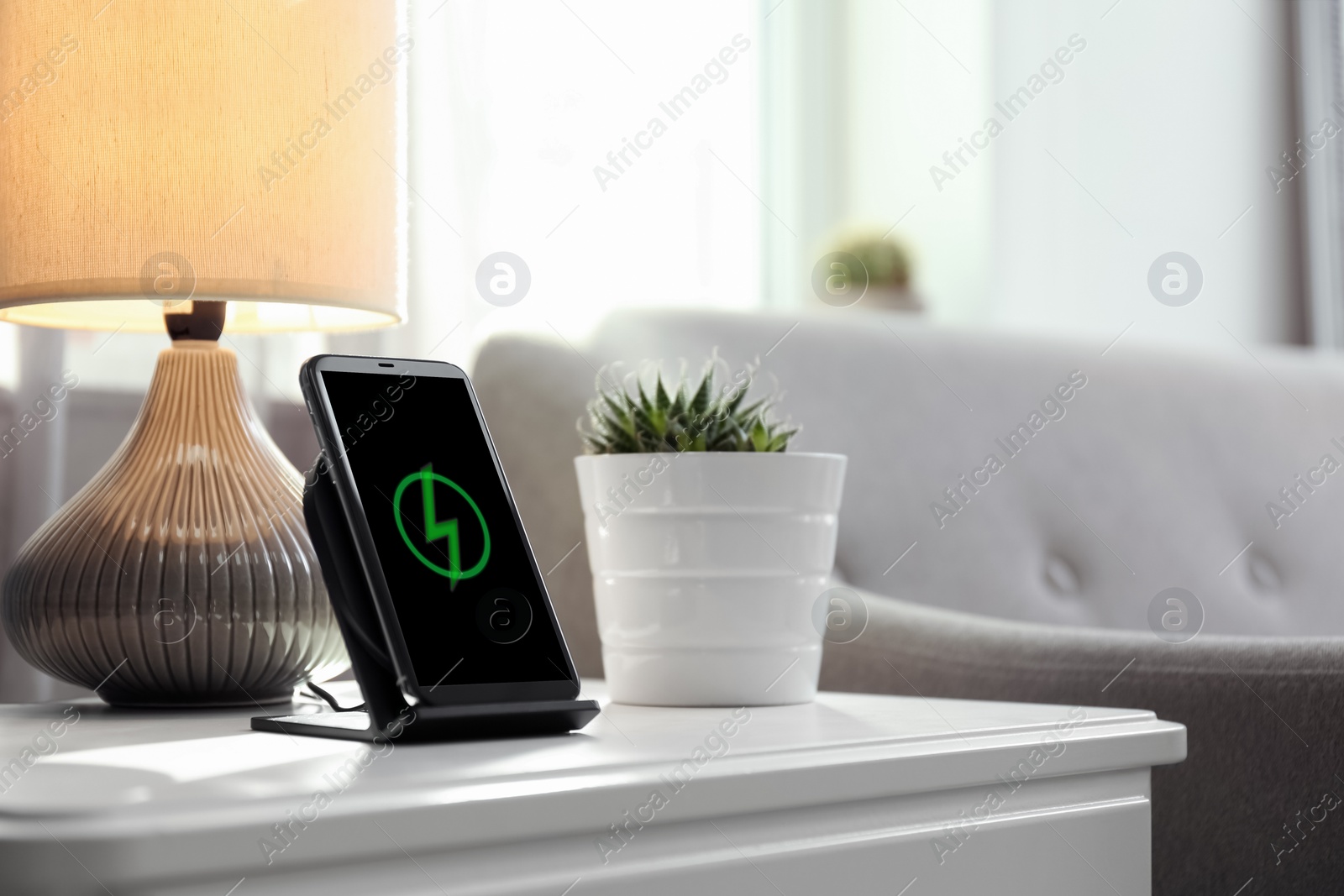 Photo of Smartphone charging on wireless pad in room. Space for text