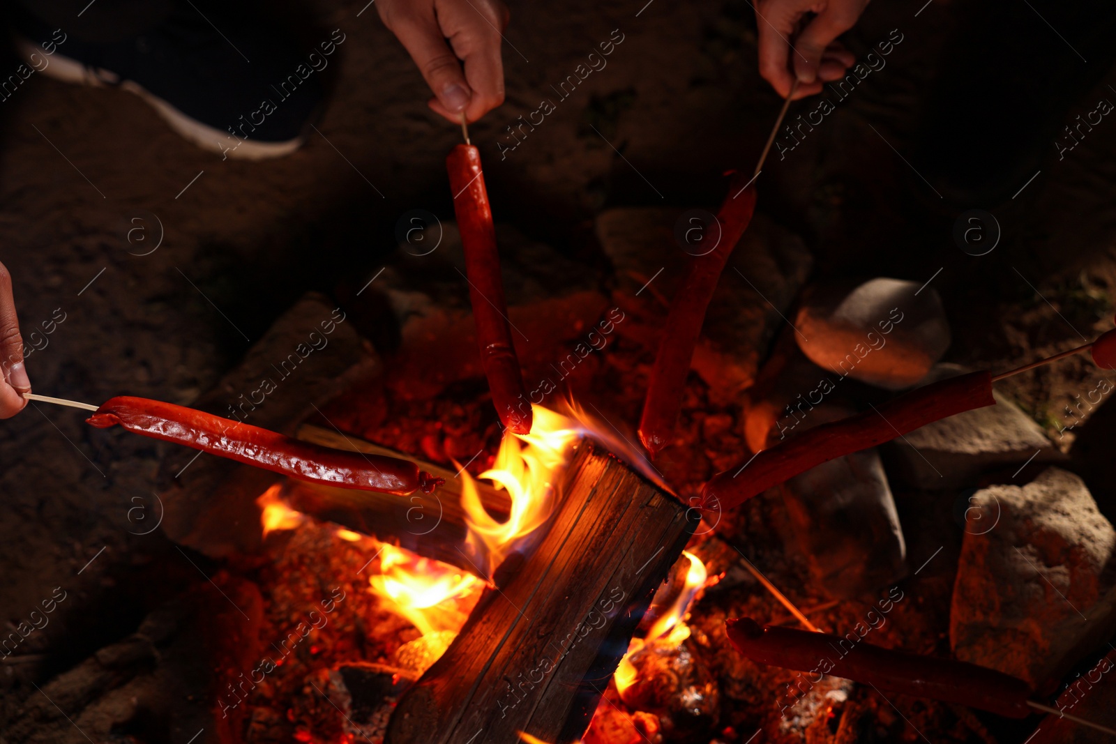 Photo of People roasting sausages on campfire outdoors at night, closeup