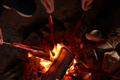 Photo of People roasting sausages on campfire outdoors at night, closeup