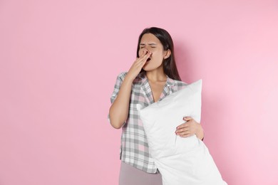 Sleepy young woman with soft pillow yawning on pink background