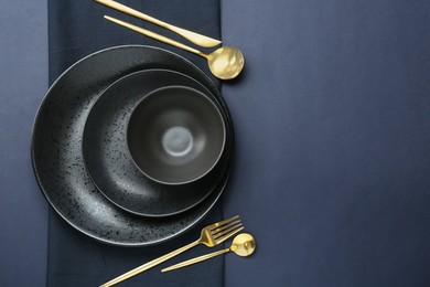 Photo of Stylish ceramic plates, bowl, cutlery and napkin on dark blue background, top view. Space for text