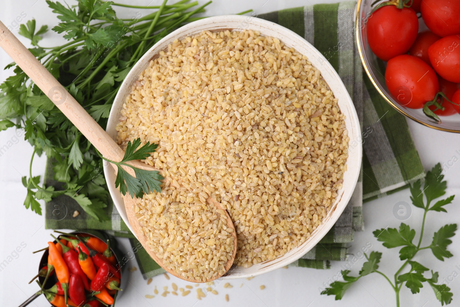 Photo of Raw bulgur in bowl, vegetables and parsley on table, flat lay