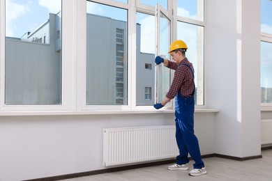 Photo of Worker in uniform installing plastic window indoors