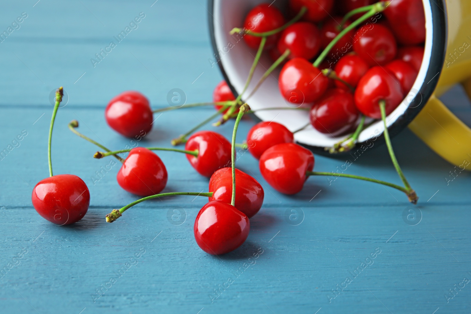 Photo of Metal mug and ripe red cherries on wooden table, closeup