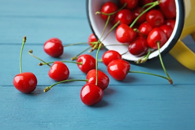 Photo of Metal mug and ripe red cherries on wooden table, closeup