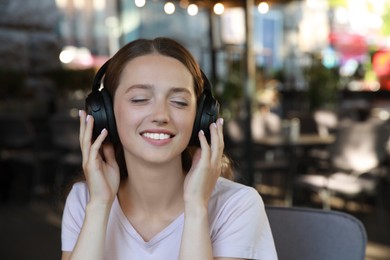 Photo of Smiling woman in headphones listening to music in outdoor cafe. Space for text