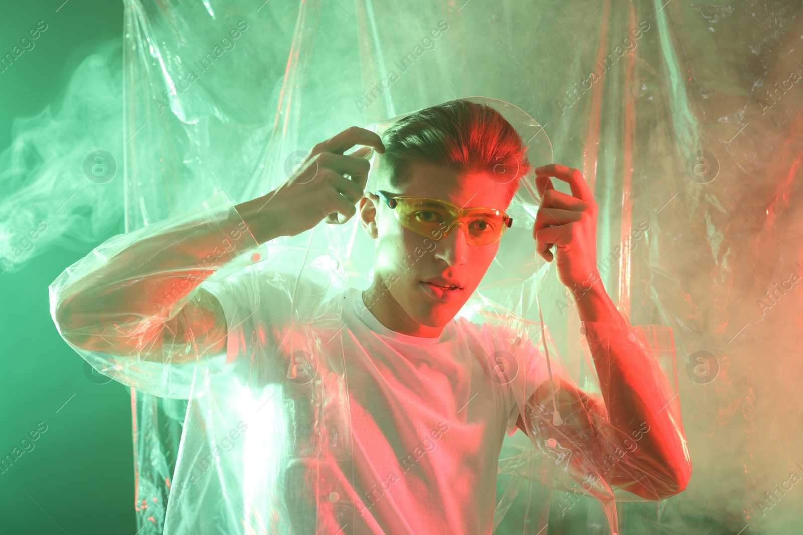 Photo of Stylish young man wearing clear coat and glasses in neon lights