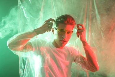 Photo of Stylish young man wearing clear coat and glasses in neon lights