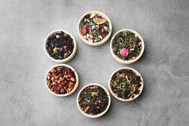 Photo of Different kinds of dry herbal tea in wooden bowls on light grey table, flat lay. Space for text