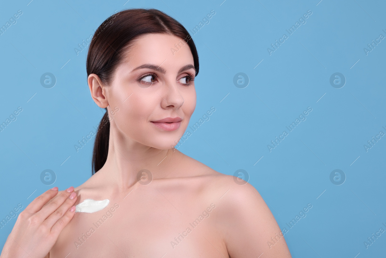 Photo of Beautiful woman with smear of body cream on her collarbone against light blue background, space for text