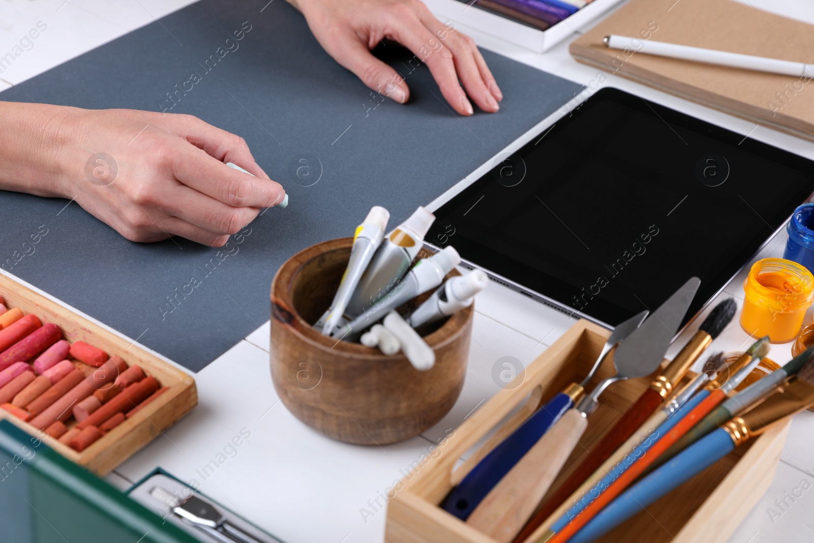 Photo of Artist drawing with chalk pastel on grey paper at white wooden table, closeup