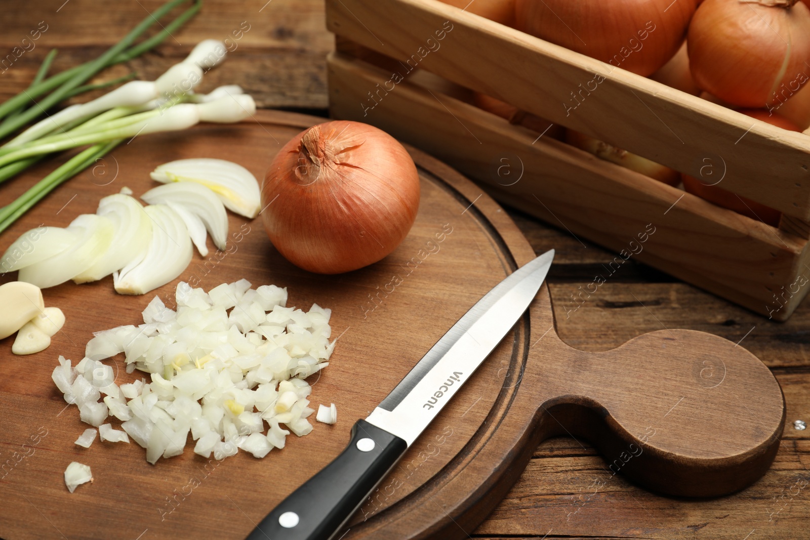 Photo of Board with cut onion and garlic on wooden table