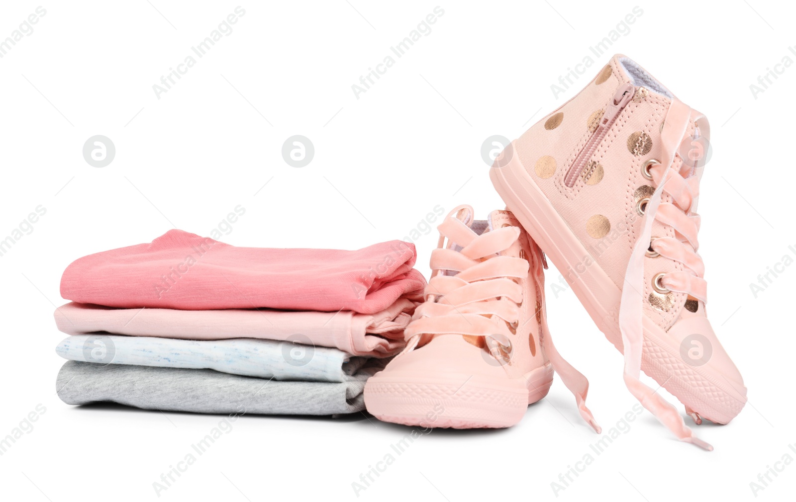 Photo of Stylish child shoes and stack of clothes on white background