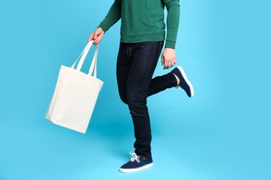 Photo of Young man with eco bag running on blue background, closeup