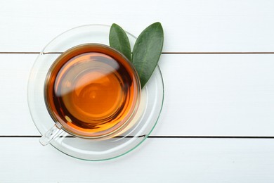 Aromatic tea in glass cup and green leaves on white wooden table, top view. Space for text