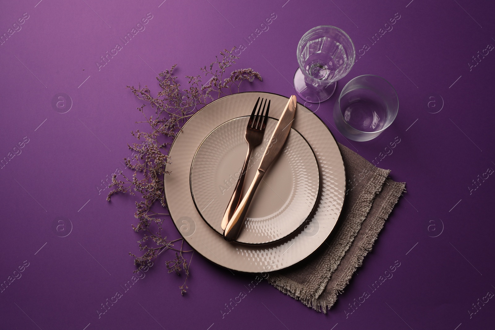 Photo of Stylish table setting. Plates, cutlery, glasses and floral decor on purple background, flat lay