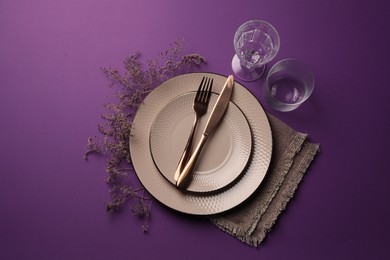 Photo of Stylish table setting. Plates, cutlery, glasses and floral decor on purple background, flat lay