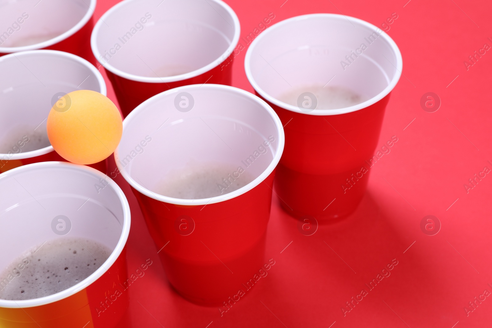 Photo of Plastic cups and ball for beer pong on red background