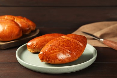 Plate with delicious baked pirozhki on wooden table