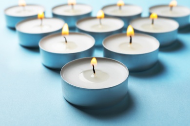 Photo of Small wax candles burning on color background, closeup