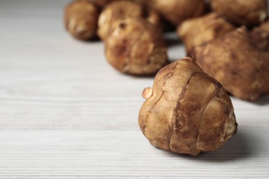 Photo of Fresh Jerusalem artichokes on white wooden table, closeup. Space for text