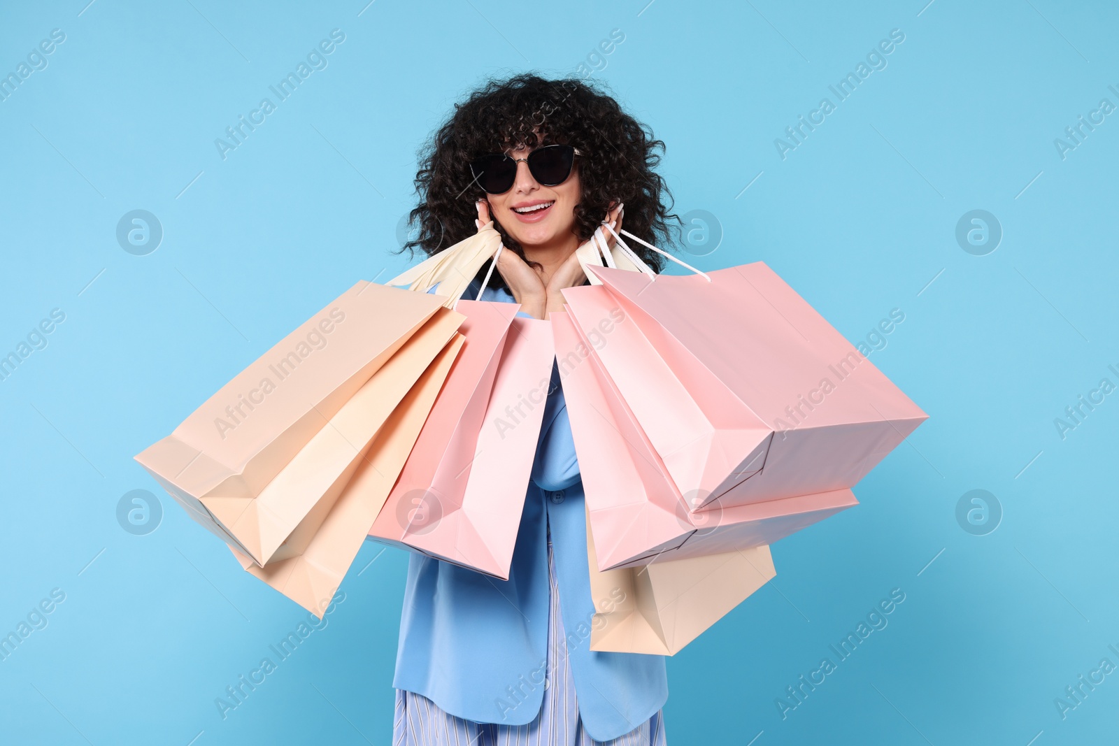 Photo of Happy young woman with shopping bags and stylish sunglasses on light blue background