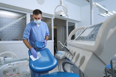 Photo of Professional dentist in uniform and medical mask cleaning workplace indoors