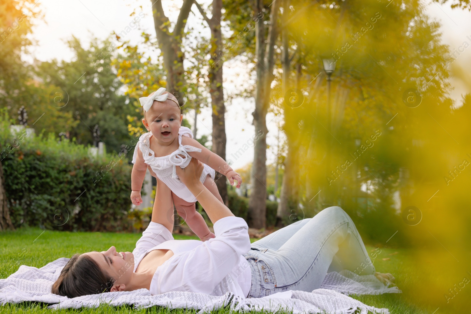 Photo of Happy mother with adorable baby lying on green grass in park