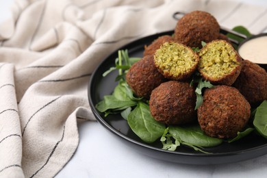 Photo of Delicious falafel balls, herbs and sauce on white table, closeup