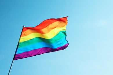 Photo of Rainbow gay flag against blue sky, space for text. LGBT concept