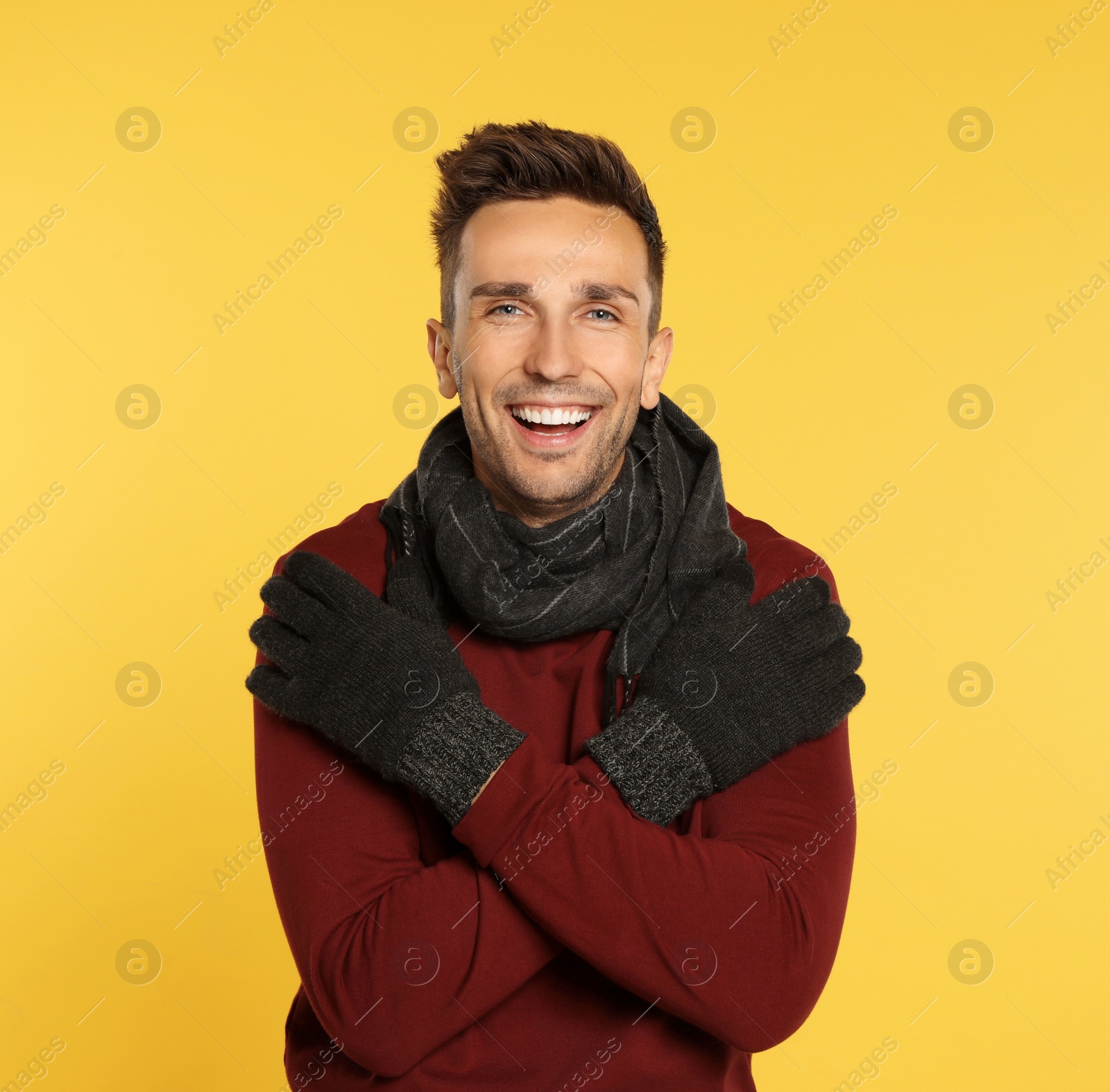 Photo of Happy young man in warm clothes on yellow background. Winter season