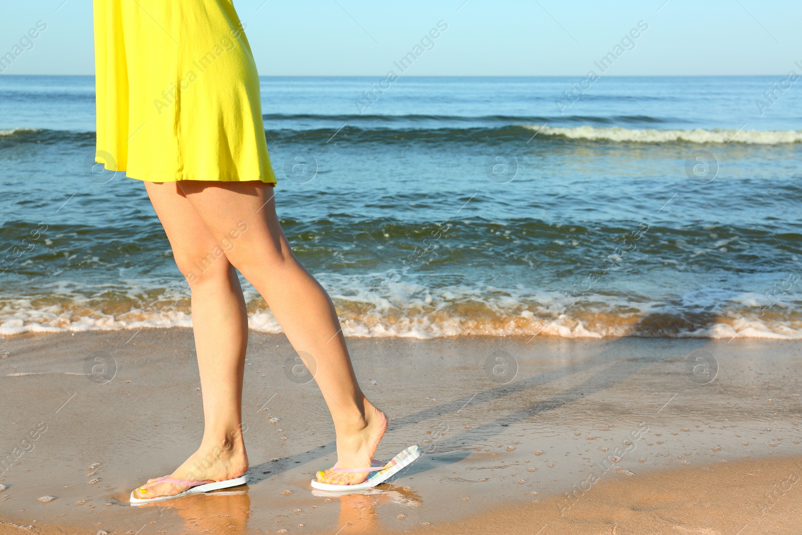 Photo of Closeup of woman with flip flops on sand near sea, space for text. Beach accessories