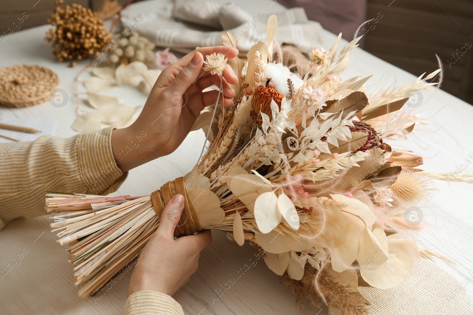 Photo of Florist making beautiful bouquet of dried flowers at white table, closeup