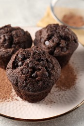 Delicious chocolate muffins and cacao powder on light grey table, closeup