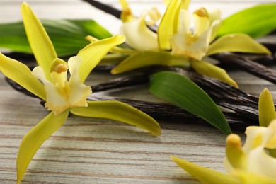 Photo of Vanilla pods, beautiful flowers and green leaves on white wooden table, closeup