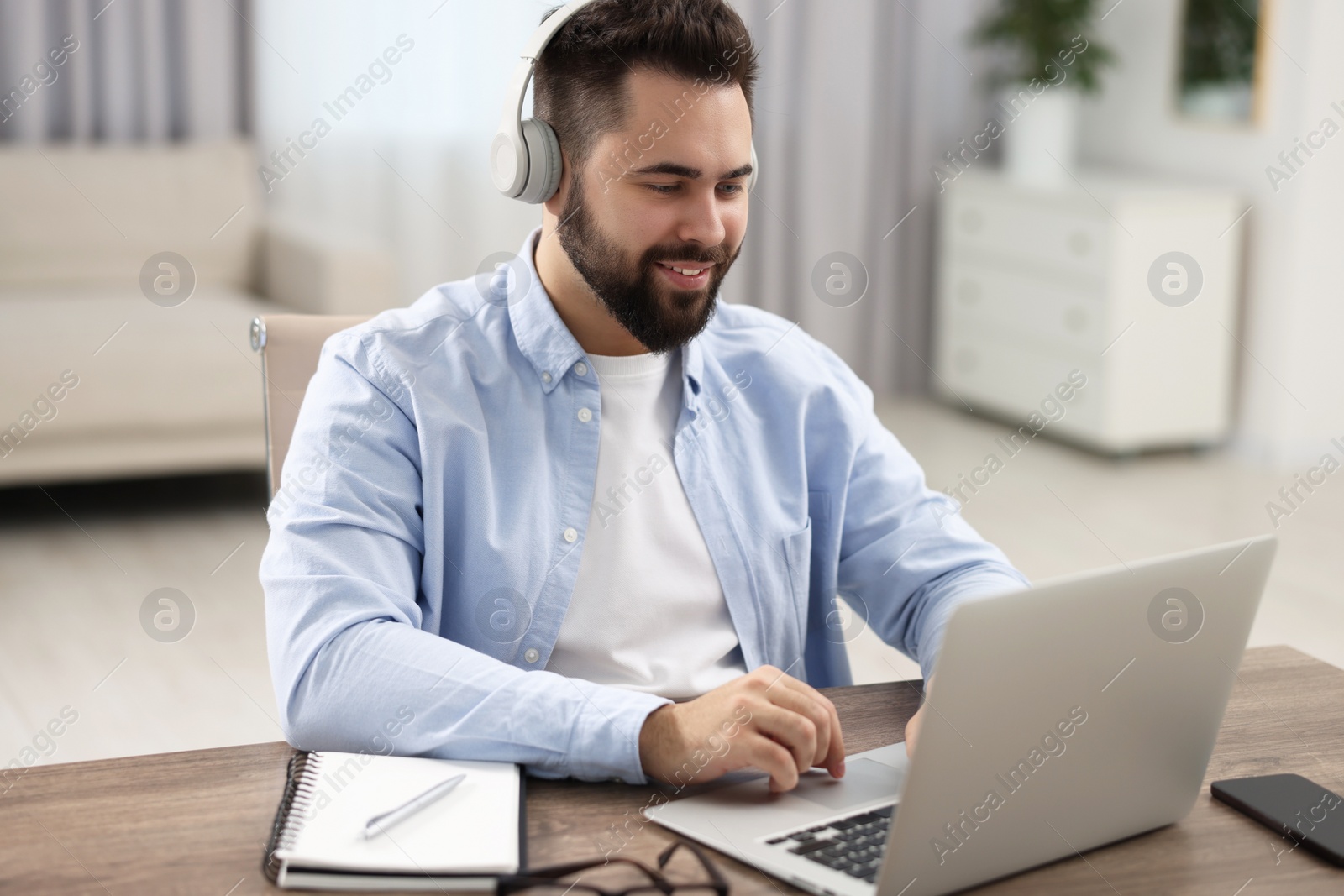 Photo of Young man in headphones watching webinar at table in room