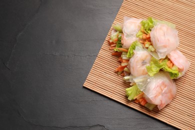 Photo of Tasty spring rolls and bamboo mat on grey textured table, top view. Space for text
