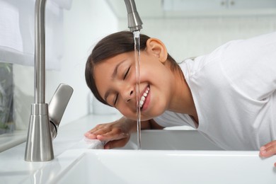 Photo of Girl drinking tap water over sink in kitchen