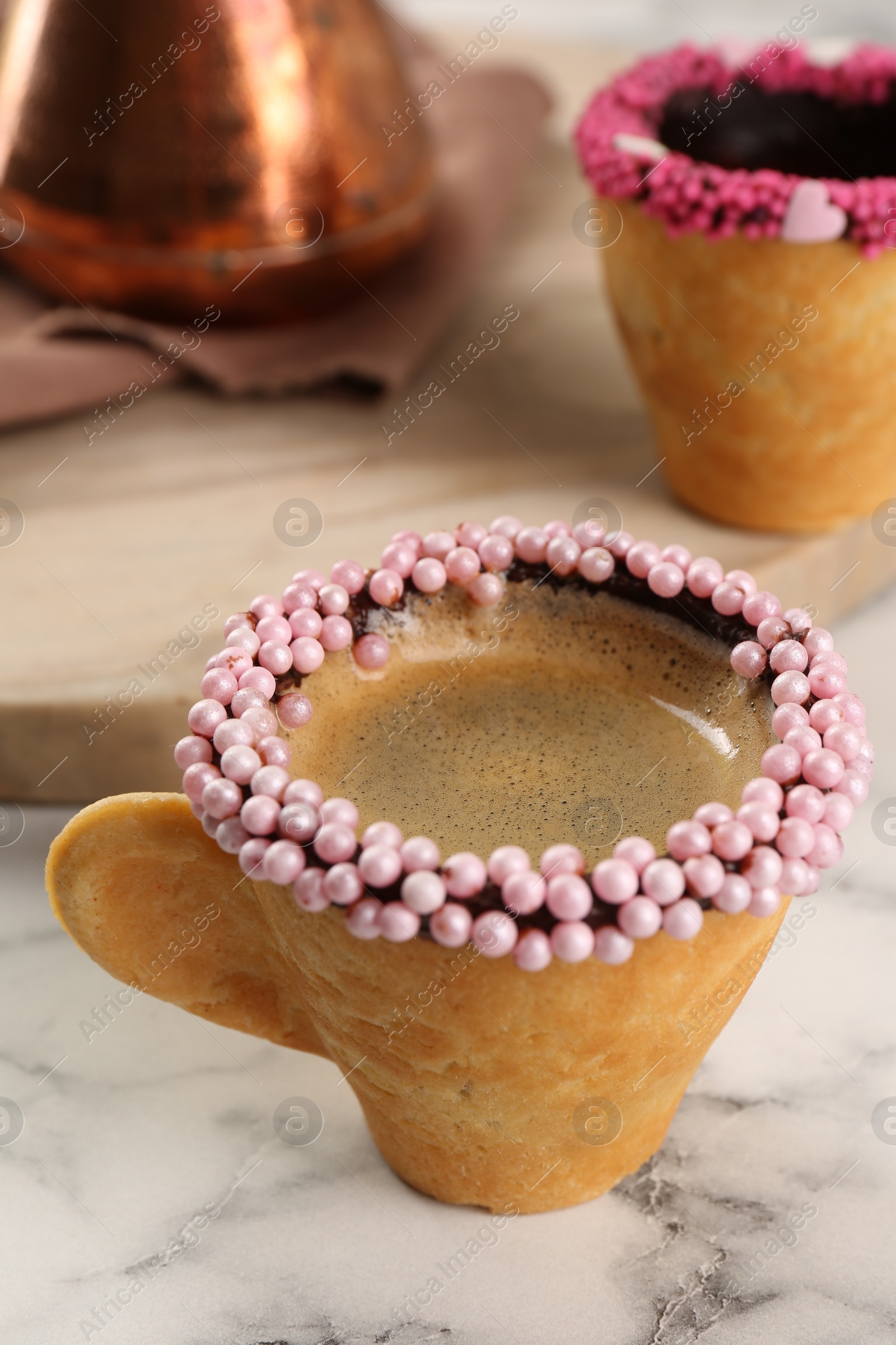 Photo of Delicious edible biscuit cup of coffee decorated with sprinkles on white marble table