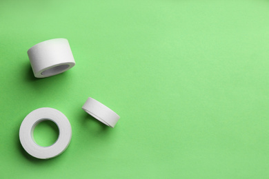 Sticking plaster rolls on green background, flat lay. Space for text