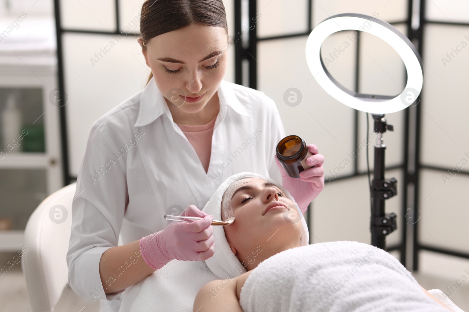 Photo of Cosmetologist applying mask on woman's face in clinic